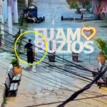 Placa informativa em Búzios danificada por vandalismo, com paisagem de praia e céu azul ao fundo.