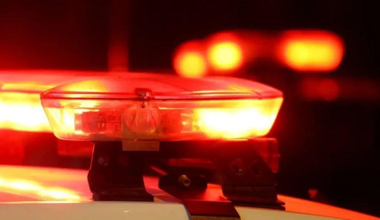 Imagem noturna de sirene de polícia com luzes azuis e vermelhas, viatura e cena de briga com motocicleta e carro, em Rio Claro, interior de SP.