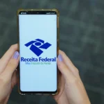 Pessoa preenchendo Imposto de Renda no computador com documentos fiscais