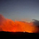 Incêndio florestal de grandes proporções no Morro do Açu, Serra dos Órgãos, com fumaça e fogo visíveis na montanha ao entardecer.