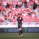 Goleiro do Internacional em jogo, defendendo uma bola, com uniforme vermelho e branco.