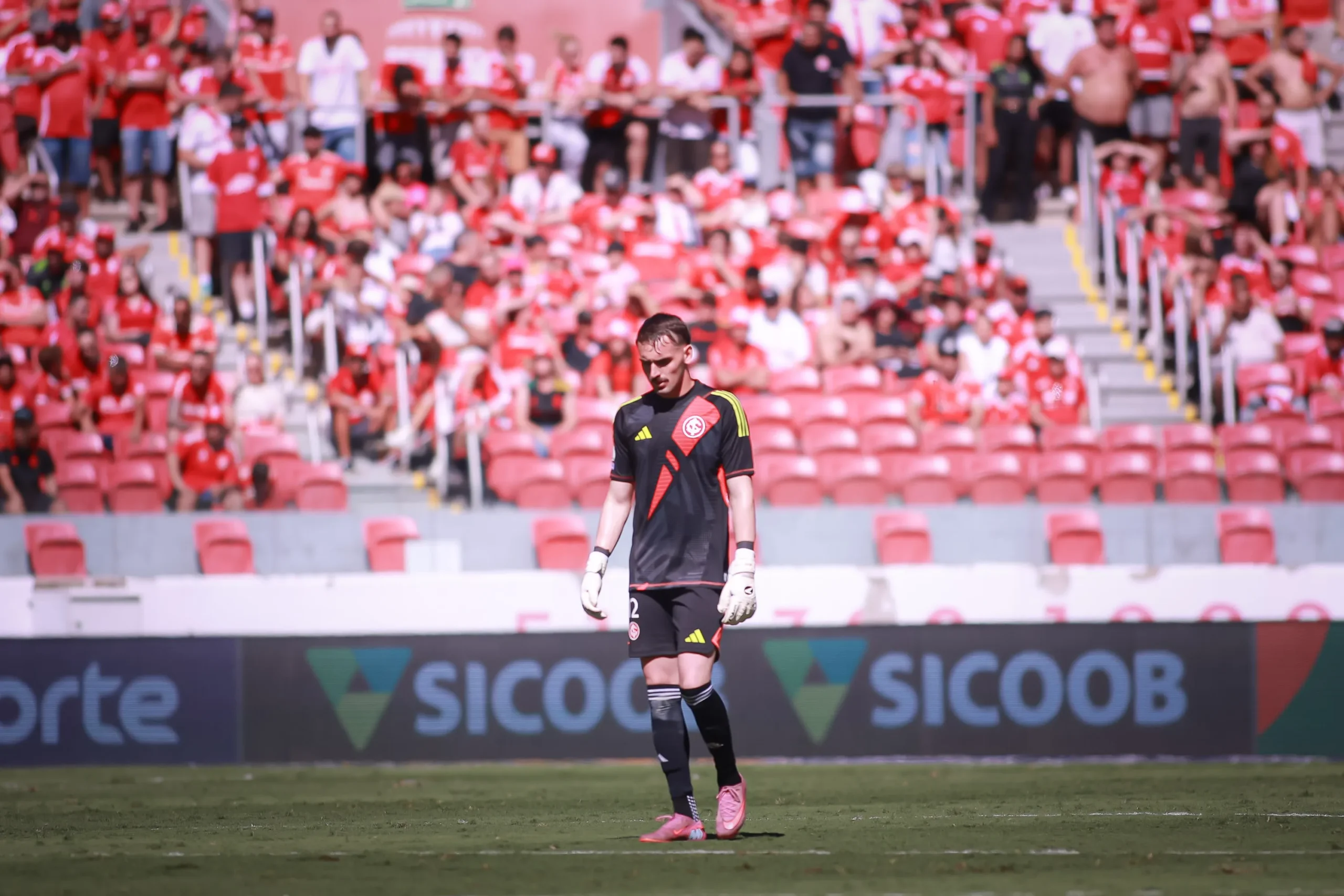 Goleiro do Internacional em jogo, defendendo uma bola, com uniforme vermelho e branco.