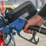 Mão segurando bico de bomba de gasolina com preços subindo e alimentos ao fundo, representando a inflação do IPCA em março.