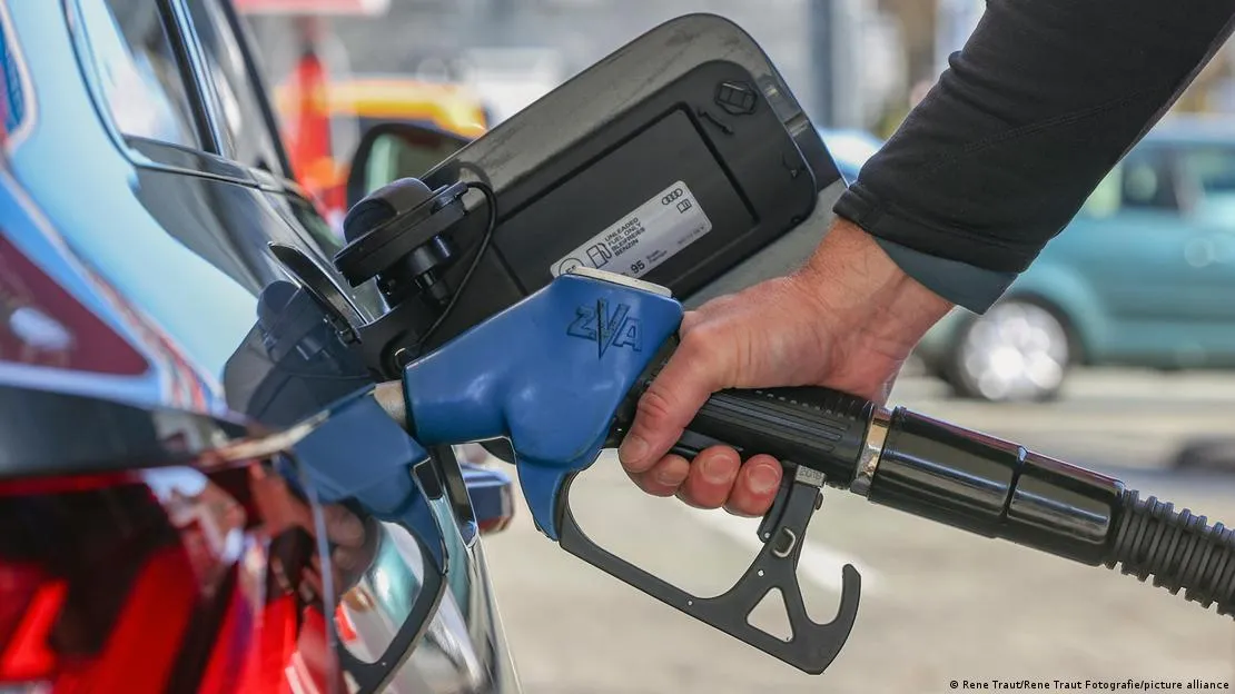 Mão segurando bico de bomba de gasolina com preços subindo e alimentos ao fundo, representando a inflação do IPCA em março.