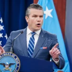 Comandante militar iraniano em uniforme, falando em televisão estatal, com bandeira do Irã ao fundo, negando ataques.