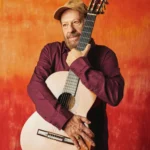 João Bosco tocando violão e sorrindo, celebrando seus 80 anos e novo álbum.