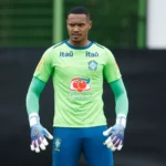 Goleiro John treinando no campo após lesão no joelho, com uniforme do Nottingham Forest, focado na recuperação e no sonho da Copa do Mundo.