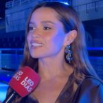 Juliette Freire, ex-BBB, sorrindo e falando em microfone, com fundo de evento de moda. Ela veste roupas modernas.