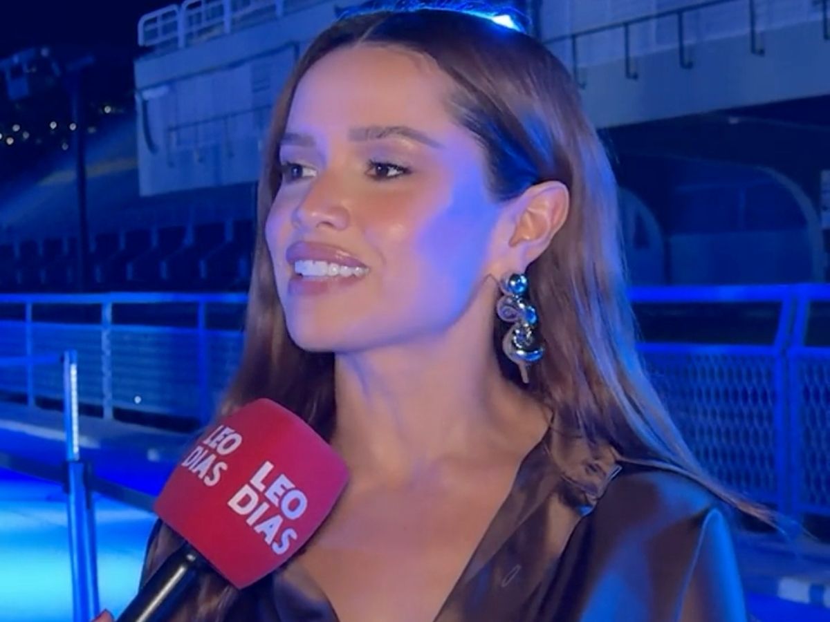 Juliette Freire, ex-BBB, sorrindo e falando em microfone, com fundo de evento de moda. Ela veste roupas modernas.