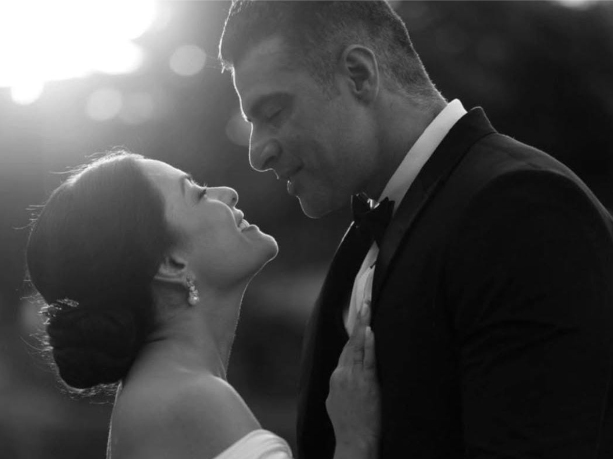 Lissa Martins cantando no palco, com lágrimas nos olhos, enquanto sua filha Antonella, de 8 anos, a observa da plateia e oferece um lencinho.