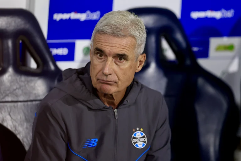 Luís Castro, técnico do Grêmio, em pé no gramado com expressão séria