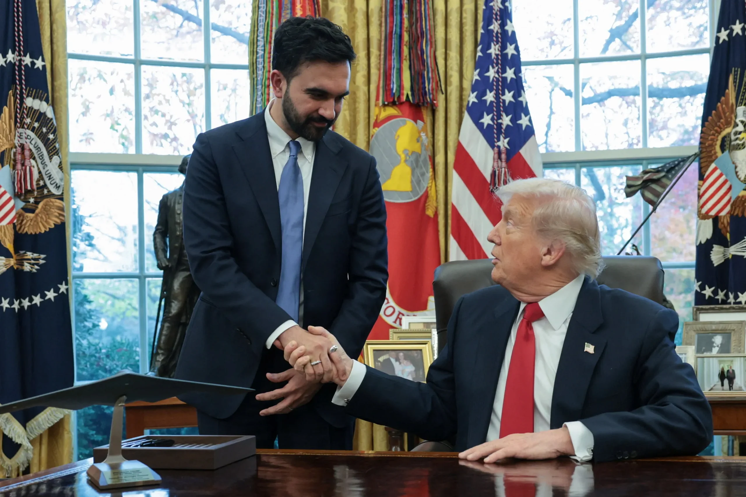 Zohran Mamdani entrega capa de jornal a Donald Trump na Casa Branca, discutindo gastos e investimentos.