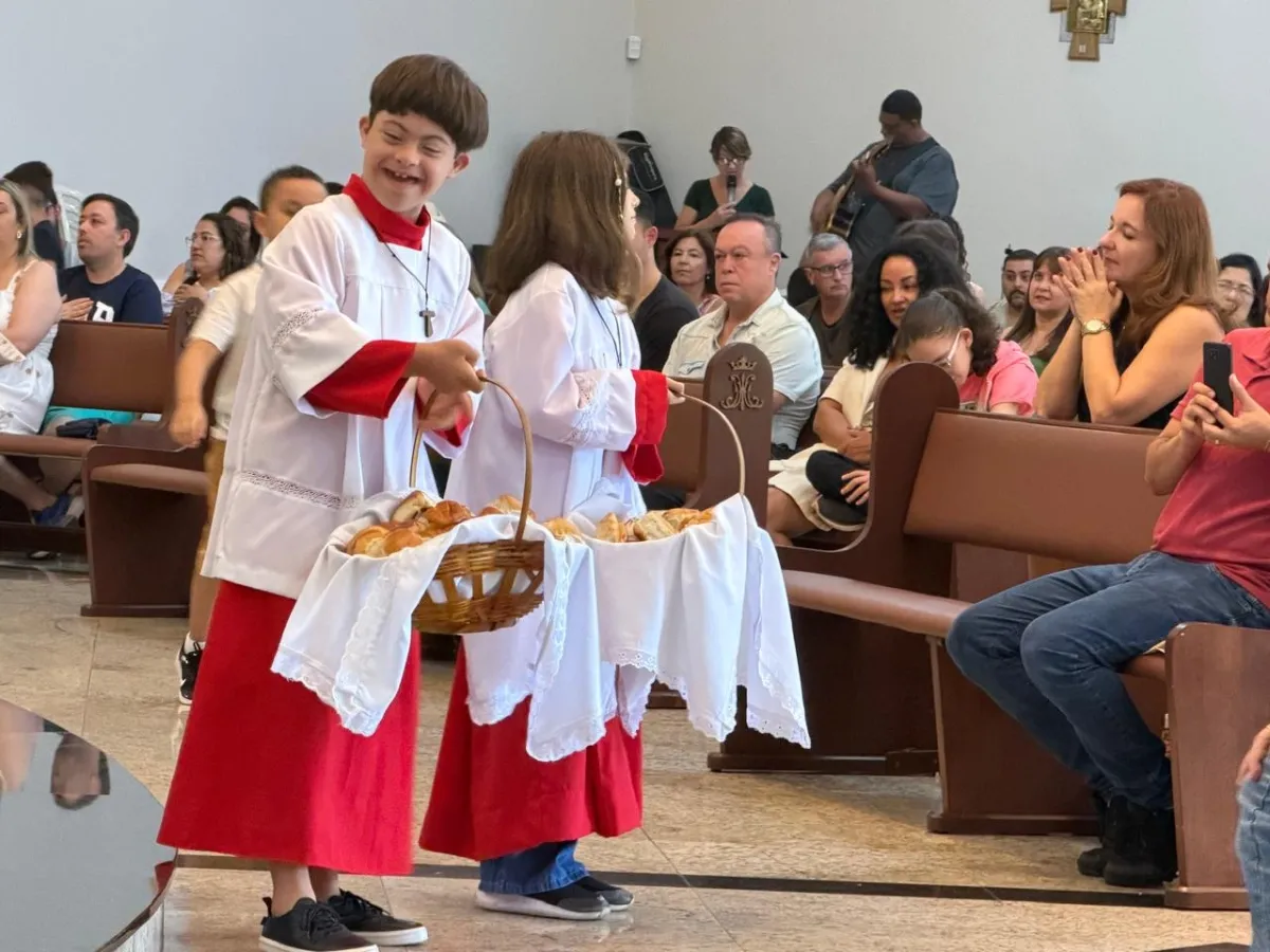 Menino com Síndrome de Down vestindo roupa de coroinha e sorrindo na igreja.