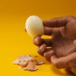 Mulher lavando alface na pia da cozinha, com frango cru em uma tábua ao lado, representando a necessidade de cuidado para não lavar carne e evitar contaminação.