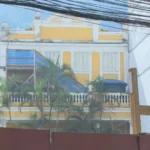 Construção de condomínio no Humaitá, Rio de Janeiro, com edifícios residenciais em andamento e a Casa Amarela ao fundo, mostrando o contexto da disputa urbanística.