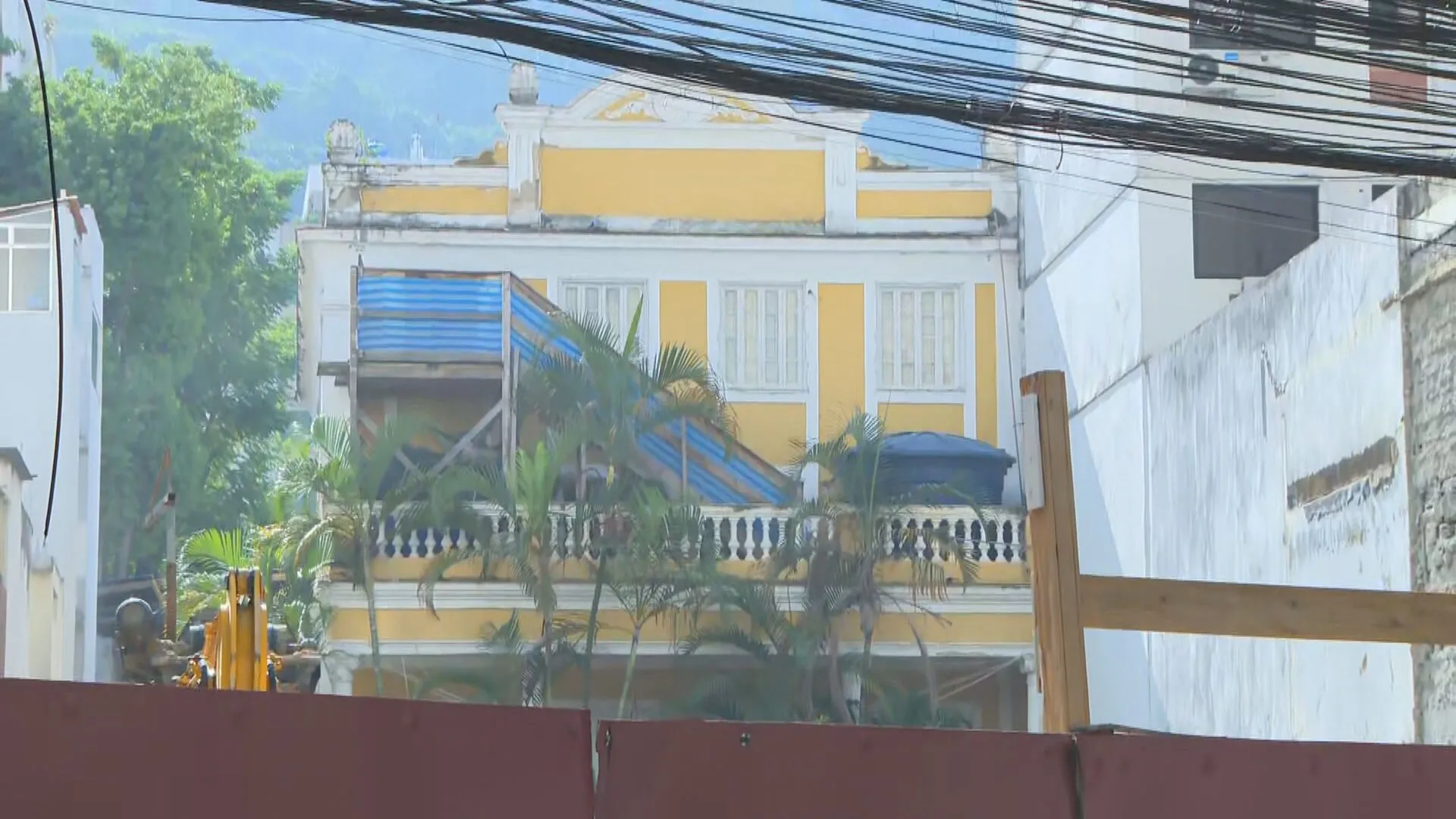 Construção de condomínio no Humaitá, Rio de Janeiro, com edifícios residenciais em andamento e a Casa Amarela ao fundo, mostrando o contexto da disputa urbanística.