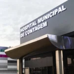 Mulher sendo socorrida no chão após ser esfaqueada em Contagem, com polícia e agressor detido ao fundo.