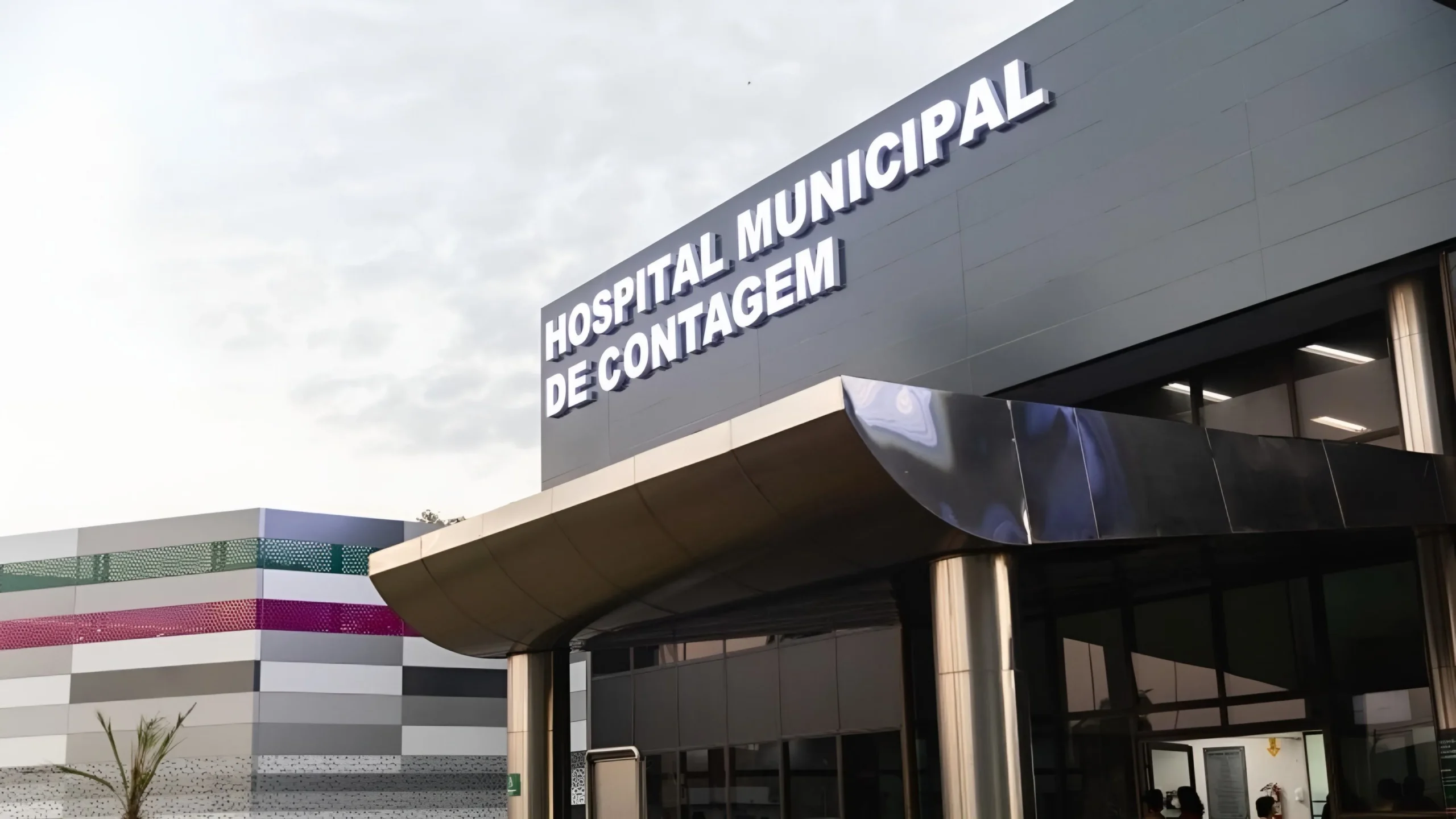 Mulher sendo socorrida no chão após ser esfaqueada em Contagem, com polícia e agressor detido ao fundo.