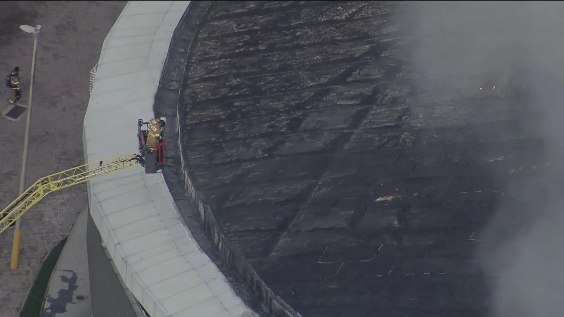 Vista noturna do Velódromo do Parque Olímpico em chamas, com bombeiros trabalhando para conter o incêndio.