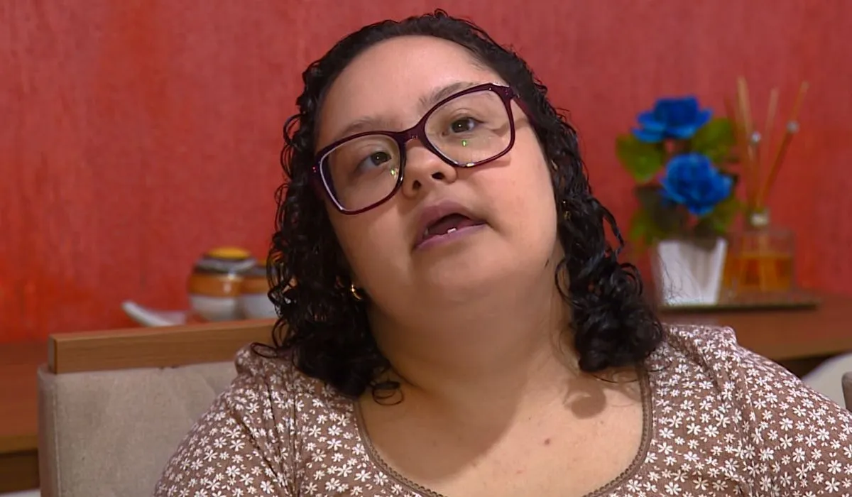 Mulher jovem com deficiência, óculos, sorrindo em ambiente de trabalho, representando inclusão e empoderamento.