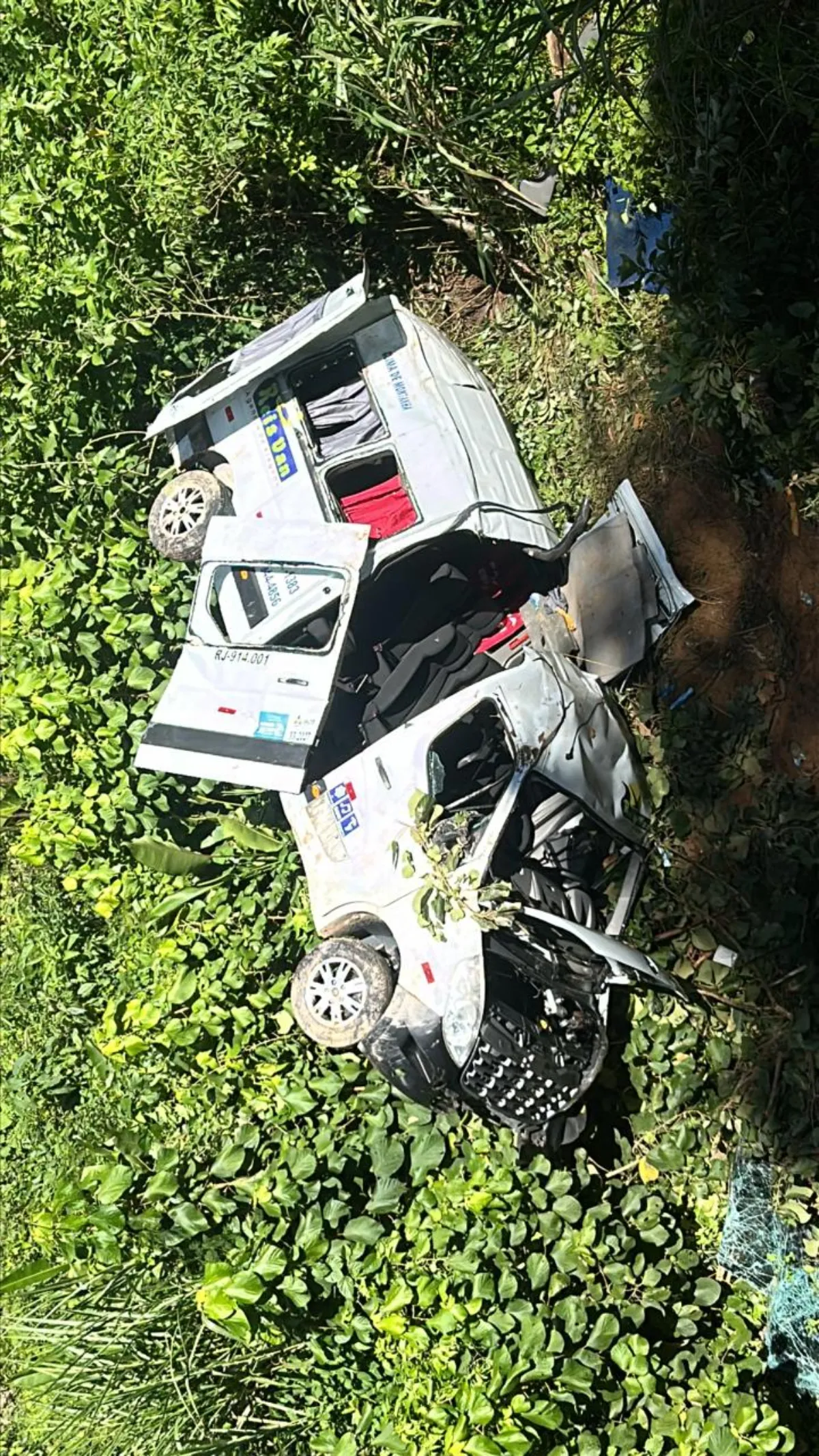 Van branca tombada em ribanceira após acidente na RJ-155 entre Angra dos Reis e Rio Claro, com socorristas e vítimas.