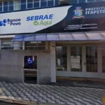 Homem e mulher jovens sorrindo, com documentos em mãos, em frente a um balcão de atendimento do PAT Itapetininga, representando a busca por emprego.