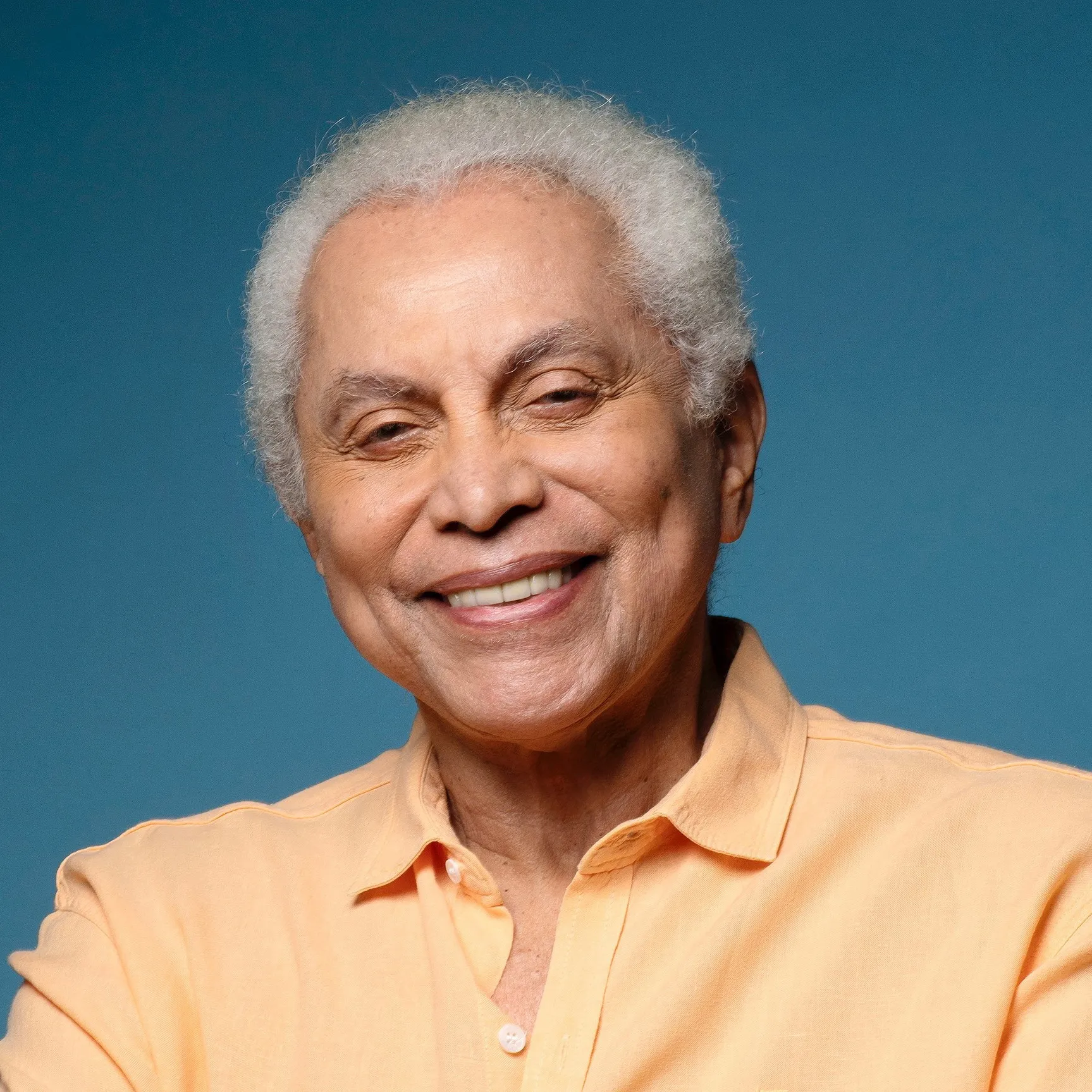 Paulinho da Viola tocando violão no palco durante um show, com iluminação de concerto