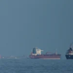 Navio-tanque de petróleo passando pelo Estreito de Ormuz com navio de guerra no horizonte
