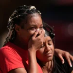 Carros de polícia e fitas de isolamento em frente a uma casa, indicando local de crime de um massacre nos EUA.