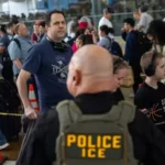 Pessoas em uma longa fila em um aeroporto dos EUA, com agentes de segurança visíveis, representando os problemas de turismo.
