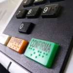 Urna eletrônica recebendo voto, com foco na mão do eleitor e fundo de pessoas diversas