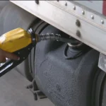 Homem abastecendo carro com diesel, com o visor da bomba mostrando preço mais baixo.