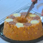 Cuscuz de linguiça em prato branco decorado com fatias de calabresa e ovo cozido