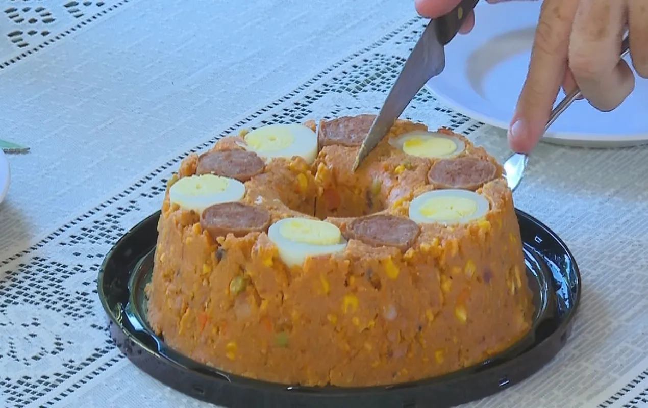 Cuscuz de linguiça em prato branco decorado com fatias de calabresa e ovo cozido