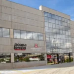 Homem em cadeira de rodas conversando com recrutador em estande de feira de empregos para PCD, com outros participantes ao fundo.