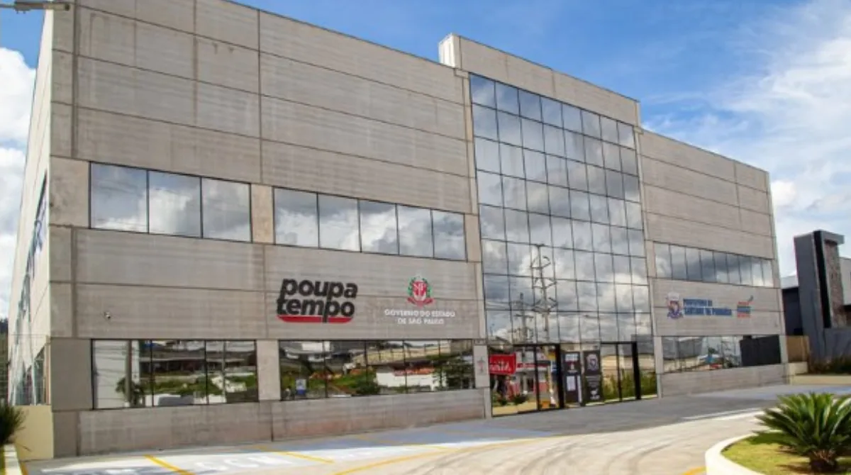 Homem em cadeira de rodas conversando com recrutador em estande de feira de empregos para PCD, com outros participantes ao fundo.