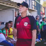 Time da Portuguesa Santista comemora o acesso à Série A2 do Campeonato Paulista, com o técnico Sérgio Guedes e jogadores abraçados em campo.