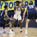 Partida de basquete entre Flamengo e Boca Juniors, jogadores em ação, ginásio lotado, placar eletrônico ao fundo