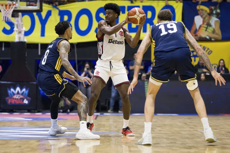 Partida de basquete entre Flamengo e Boca Juniors, jogadores em ação, ginásio lotado, placar eletrônico ao fundo