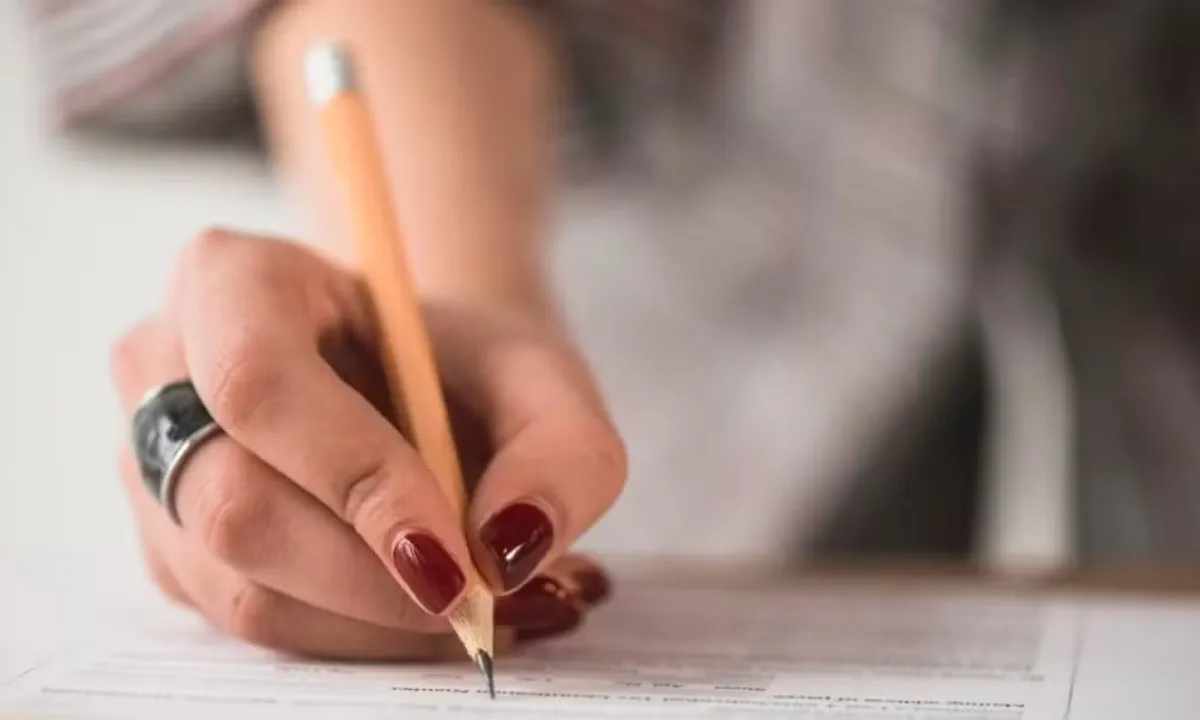 Pessoa estudando para concursos no Sul de Minas, livros abertos, notebook, canetas, preparação para prova.