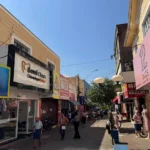 Pessoas em rua comercial movimentada durante feriado de Tiradentes, com lojas abertas e movimento de pedestres.