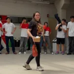 Professora Tatiane Sandmann sendo aplaudida por alunos em corredor de homenagem na escola.