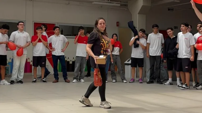 Professora Tatiane Sandmann sendo aplaudida por alunos em corredor de homenagem na escola.