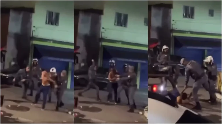 Homem no chão sendo contido por policiais militares em rua escura, com outros policiais próximos. Cena de violência policial.