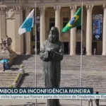 Apresentador do programa Notícias RJ2 em estúdio, com mapa do Rio ao fundo.