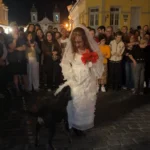 Vira-lata no teatro de rua, puxando vestido de atriz durante peça dramática.