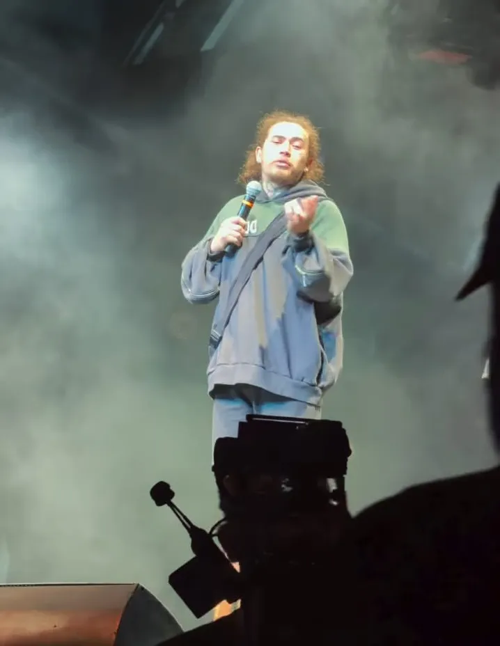 Whindersson Nunes sorrindo no palco, em frente a um ringue de boxe, com luvas, fazendo piada sobre Popó e sua família